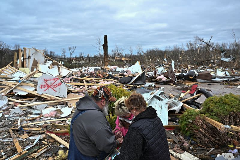 Un hombre reza con Debbie Lowdermilk y Jodee Minks al ver su escuela destruida el día después de que un tornado azotara Sullivan, Indiana, EEUU