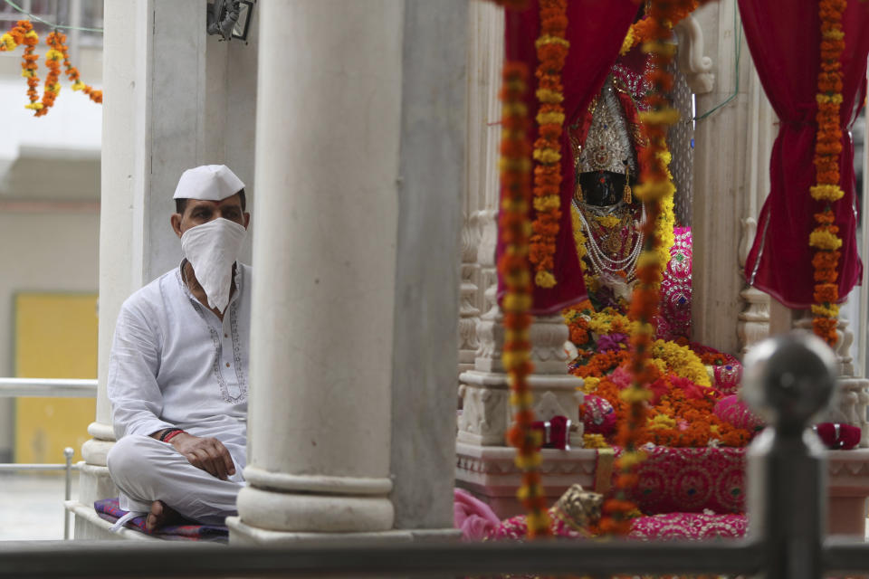 A priest wearing a mask sits to perform rituals during the annual festival at Kheer Bhawani temple amid the Coronavirus pandemic in Jammu, India, Saturday, May 30, 2020. The festival was marked in a low key manner due to the lockdown to prevent the spread of the new coronavirus. (AP Photo/Channi Anand)