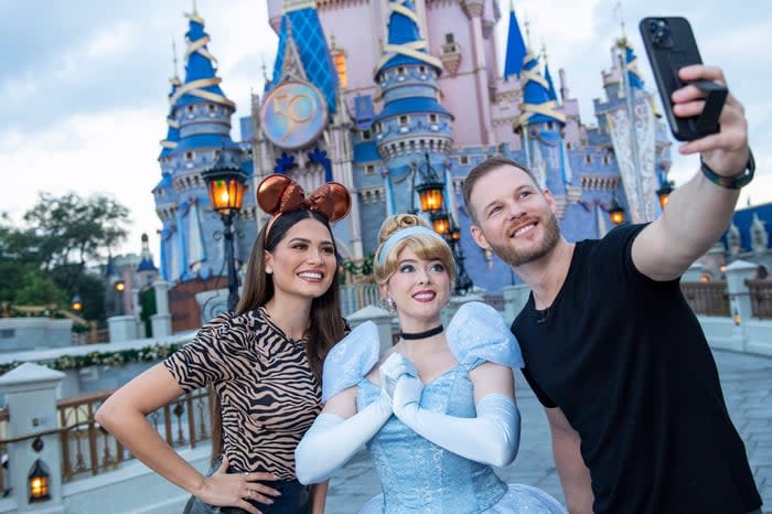 Celebrities pose with Cinderella in front of her theme park castle.