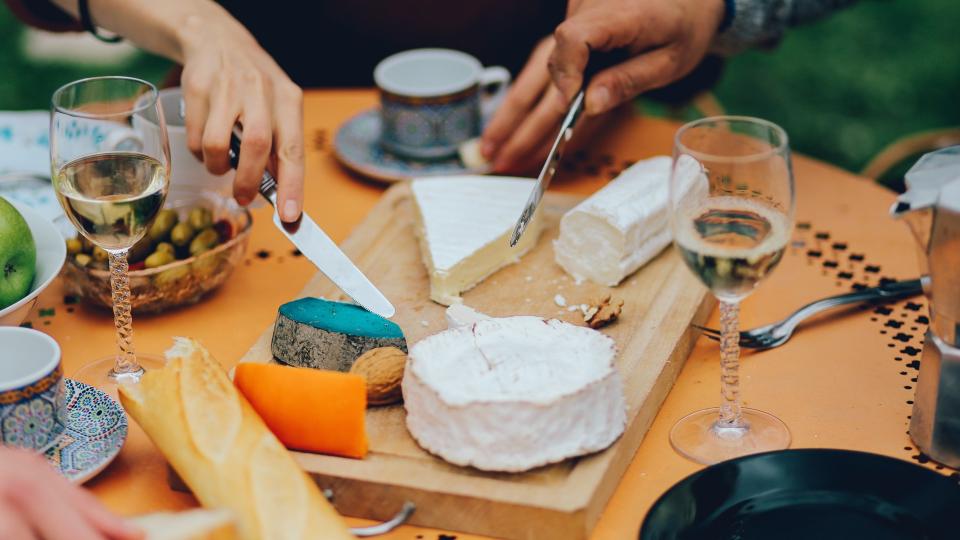 Vintage toned close up image of the table in the garden of a Paris suburban home, filled with traditional French food, different types of cheese, wine, home made baguette bread, and fruits and vegetables.