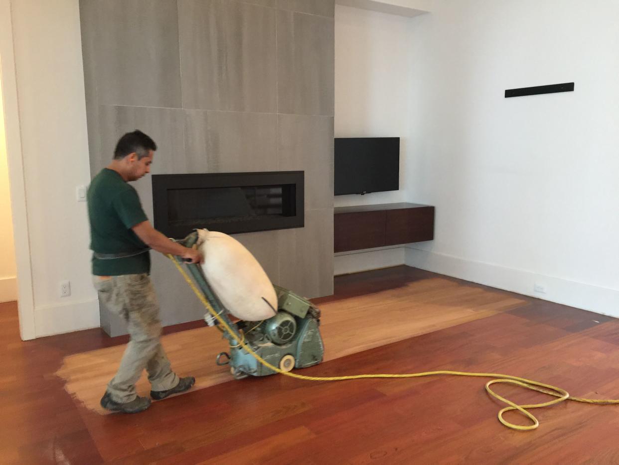 Construction worker sanding a wood floor inside home.