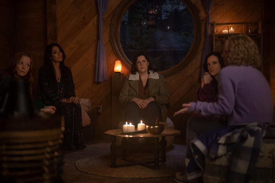 A group of adult women sit around a round coffee table with candles on it; still from "Yellowjackets"
