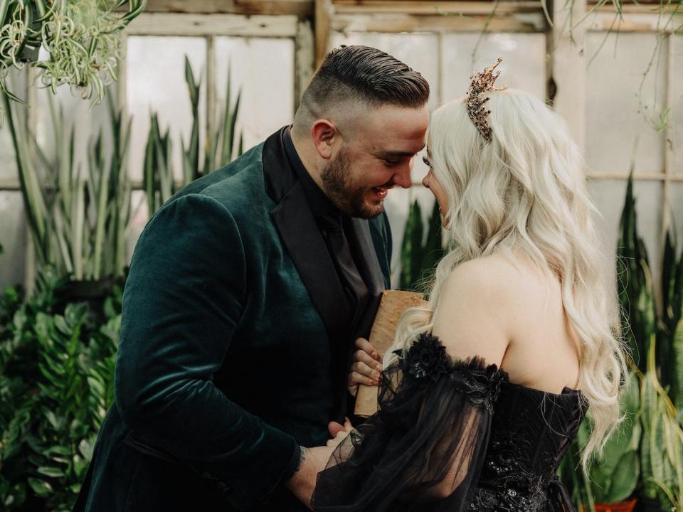 A bride and groom lean their heads together in a green house.