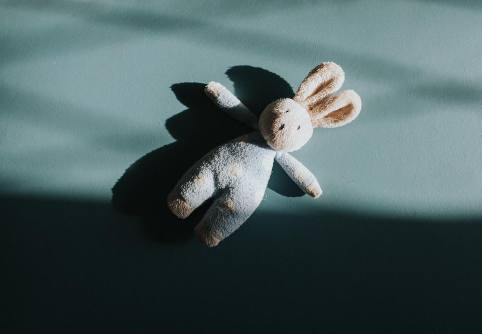 A stuffed rabbit lies on a flat surface, partially in the shade