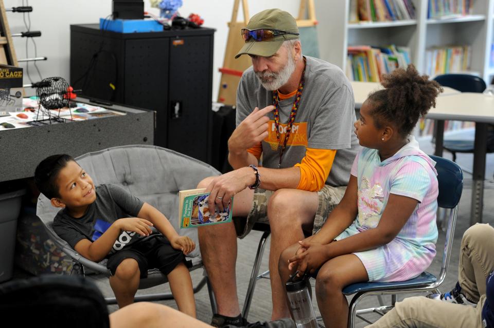 Group leader Kenneth Curtin reads to Jefferson Ponce, 7, left, and Ashley Hiraldo, 6, at the Hoops and Homework site at 12 Interfaith Terrace in Framingham, July 12, 2022.