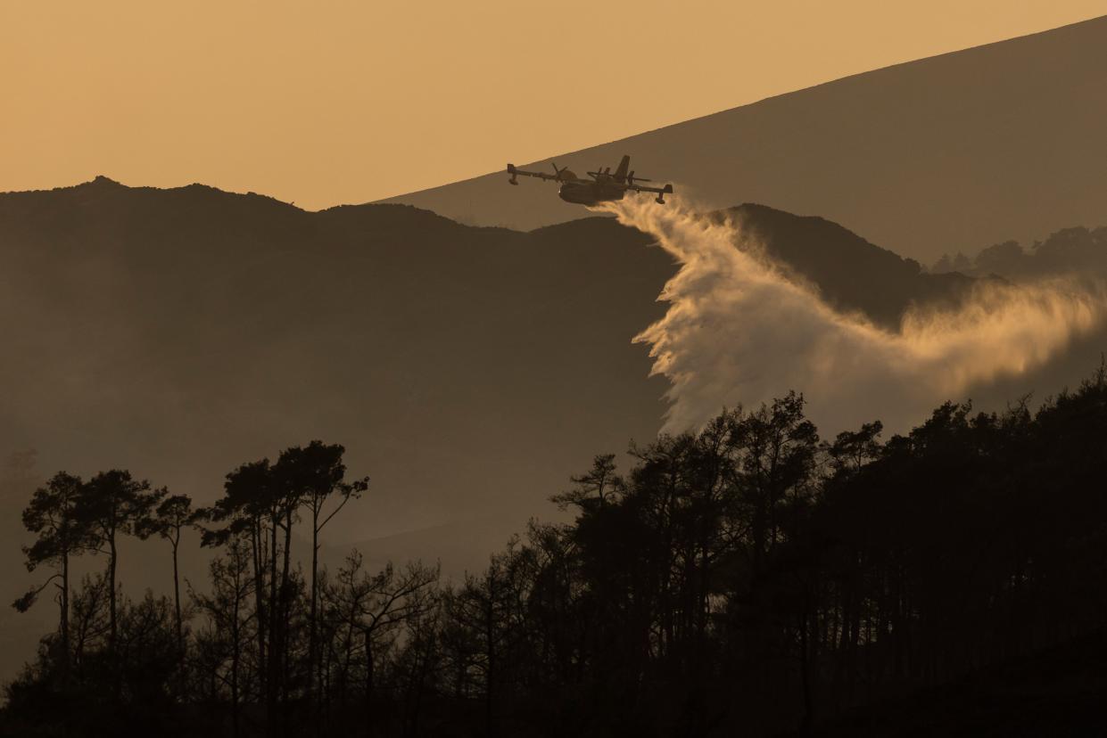 A plane drops water onto flames on a hillside at sunset on July 27, 2023 in Vati, Rhodes (Getty Images)
