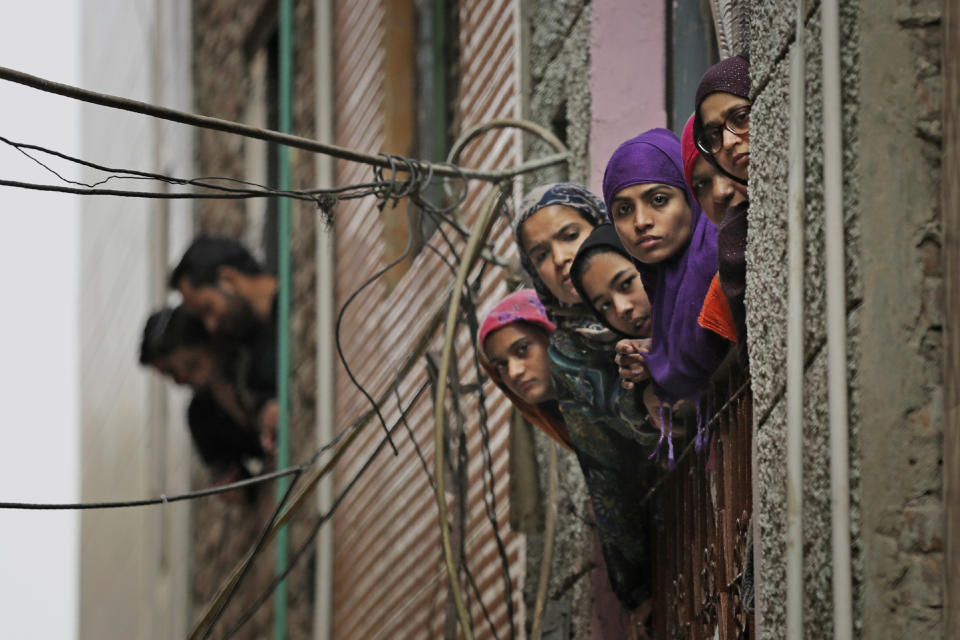 Indian Muslim women look out of a window as security officers patrol a street in New Delhi, India, Wednesday, Feb. 26, 2020. At least 20 people were killed in three days of clashes in New Delhi, with the death toll expected to rise as hospitals were overflowed with dozens of injured people, authorities said Wednesday. The clashes between Hindu mobs and Muslims protesting a contentious new citizenship law that fast-tracks naturalization for foreign-born religious minorities of all major faiths in South Asia except Islam escalated Tuesday. (AP Photo/Altaf Qadri)