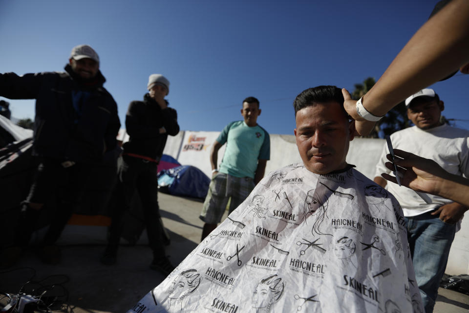 In this Dec. 3, 2018 photo, Honduran migrant barber Daniel Villafranca, 19, cuts the hair of fellow migrant Juan Francisco Medrano as other clients wait their turn inside the former concert venue Barretal, now serving as a shelter for more than 2,000 migrants, in Tijuana, Mexico. Facing the possibility of a months-long wait in Tijuana before even having an opportunity to request asylum in the United States, members of the migrant caravans that have arrived in Tijuana are looking for work. Some are creating their own informal businesses. (AP Photo/Rebecca Blackwell)