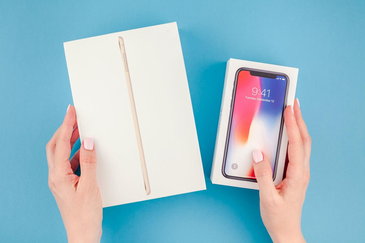 Woman hands holding boxes of the latest Apple iPhone X 10 smartphone and Ipad mini against bright blue background.