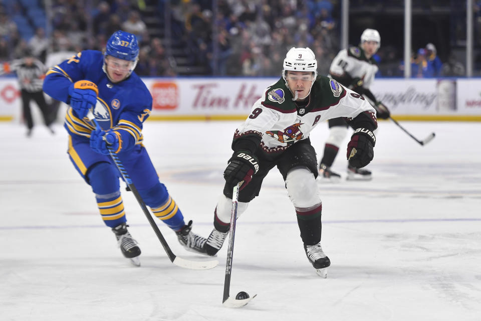 Arizona Coyotes right wing Clayton Keller, right, reaches for the puck in front of Buffalo Sabres center Casey Mittelstadt during the first period of an NHL hockey game in Buffalo, N.Y., Monday, Dec. 11, 2023. (AP Photo/Adrian Kraus)