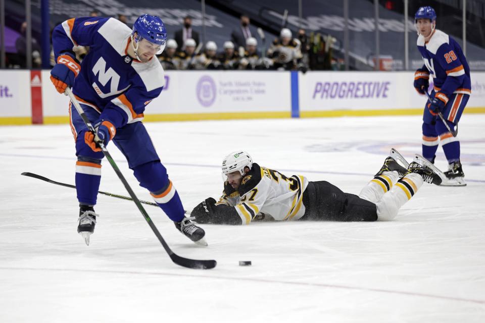Boston Bruins center Patrice Bergeron (37) slides on the ice behind New York Islanders defenseman Adam Pelech during the third period of an NHL hockey game Saturday, Feb. 13, 2021, in Uniondale, N.Y. The Islanders won 4-2. (AP Photo/Adam Hunger)