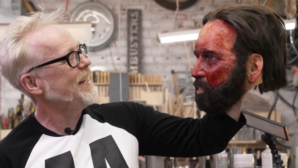 Adam Savage holds up a latex mask of Nicolas Cage