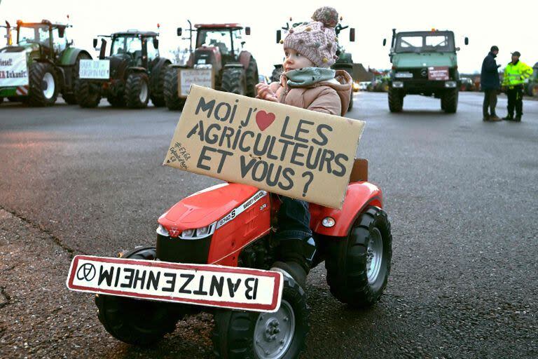 La hija de un granjero viaja en un tractor para niños con un cartel que dice “Yo, amo a los agricultores, ¿y tú?” Durante una manifestación en la frontera franco-alemana en Ottmarsheim, este de Francia, el 1 de febrero de 2024. (Foto de PATRICK HERTZOG / AFP)