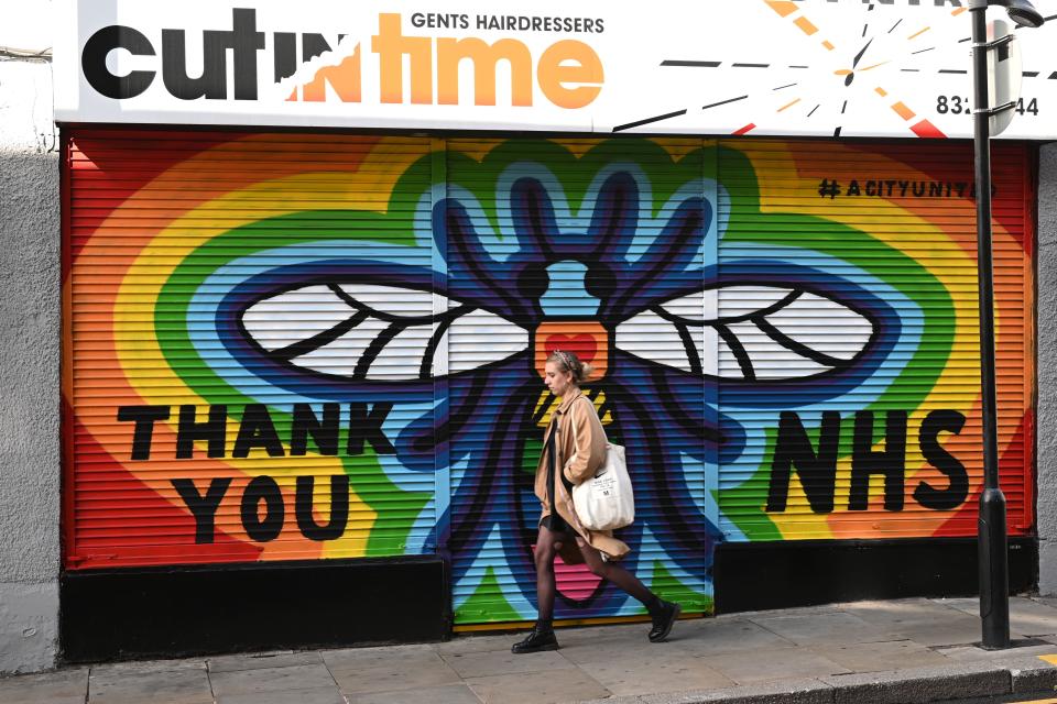 A woman walks past graffiti in praise of the NHS (national health service) on the shutters of a closed hairdressers shop in central Manchester on June 5, 2020, as lockdown measures are eased during the novel coronavirus COVID-19 pandemic. (Photo by Oli SCARFF / AFP) (Photo by OLI SCARFF/AFP via Getty Images)