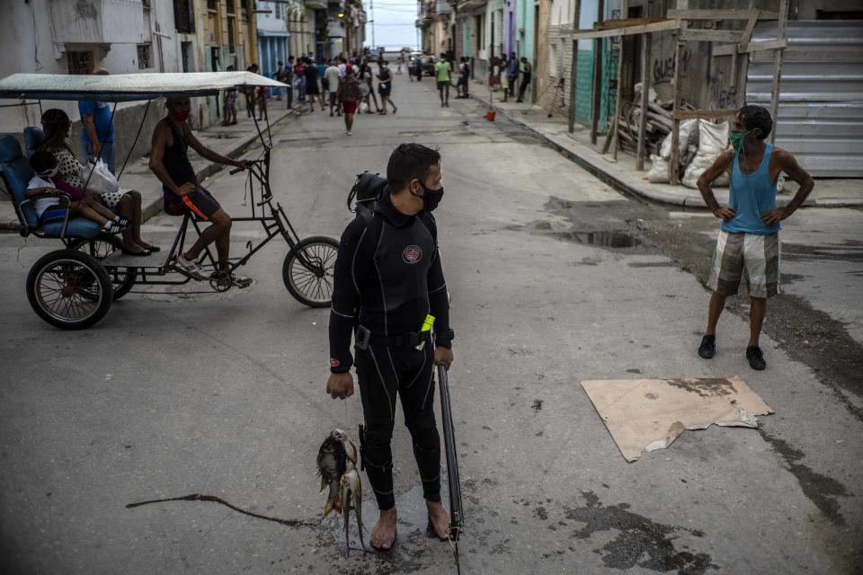 Con una máscara facial en medio de la pandemia del nuevo coronavirus, el buzo Yuniel González camina a casa con su pesca del día en La Habana, Cuba, el martes 27 de octubre de 2020. (AP Foto/Ramón Espinosa)