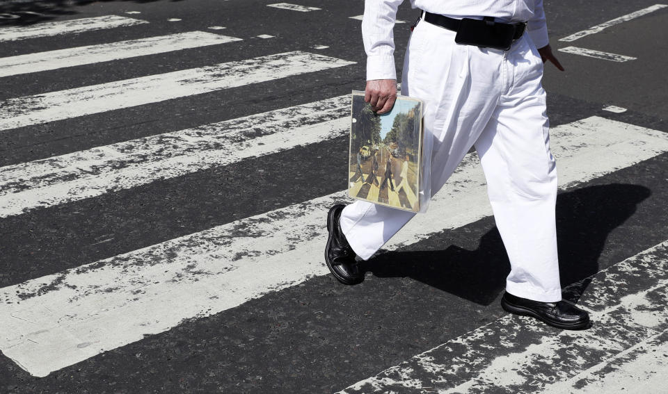 A fan carries a copy of the album 'Abbey Road' as he crosses the Abbey Road zebra crossing on the 50th anniversary of British pop musicians The Beatles doing it for their album cover of 'Abbey Road' in St Johns Wood in London, Thursday, Aug. 8, 2019. They aimed to cross 50 years to the minute since the 'Fab Four' were photographed for the album cover. (AP Photo/Kirsty Wigglesworth)