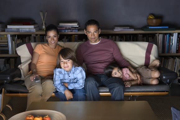 A family on a sofa watches TV.