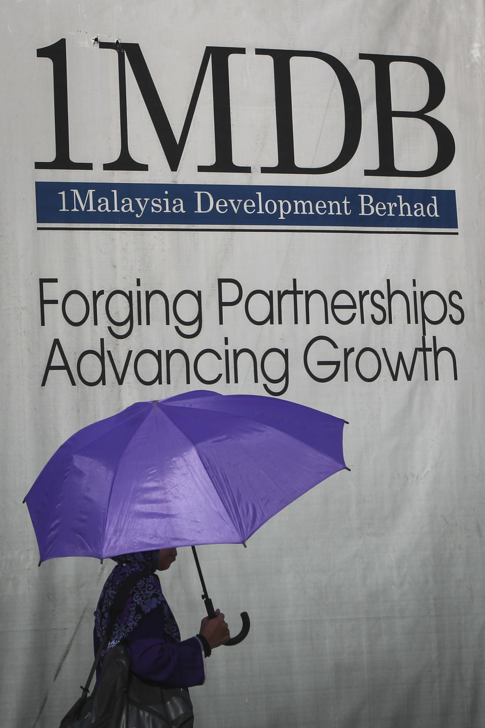 A Malaysian Muslim woman walks past a 1Malaysia Development Berhad (1MDB) billboard at the flagship's development site in Kuala Lumpur, Malaysia, July 8, 2015. Najib Razak on Tuesday, Aug. 23, 2022 was Malaysia’s first former prime minister to go to prison -- a mighty fall for a veteran British-educated politician whose father and uncle were the country’s second and third prime ministers, respectively. The 1MDB financial scandal that brought him down was not just a personal blow but shook the stranglehold his United Malays National Organization party had over Malaysian politics. (AP Photo/Joshua Paul)