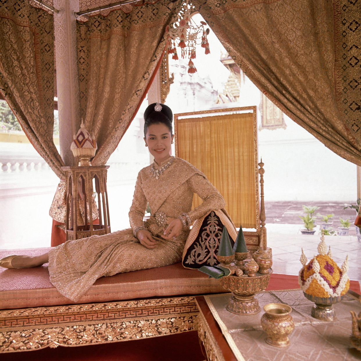 H.M. Queen Sirikit, seated on gold leafed bed in the King's coronation pavilion, wearing a dress of twenty-carat gold embossed crystal, with diamonds, which she wore to the Greek Royal wedding and was designed for her by Pierre Balmain, and diamond and gold jewelry. (Photo by Henry Clarke/Condé Nast via Getty Images)