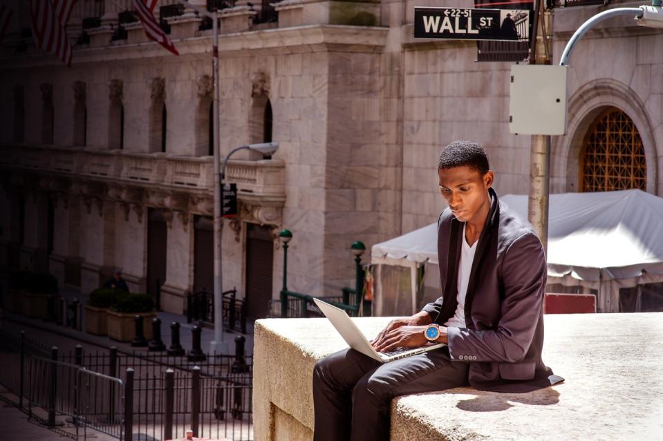 Person with laptop working outdoors on Wall Street.