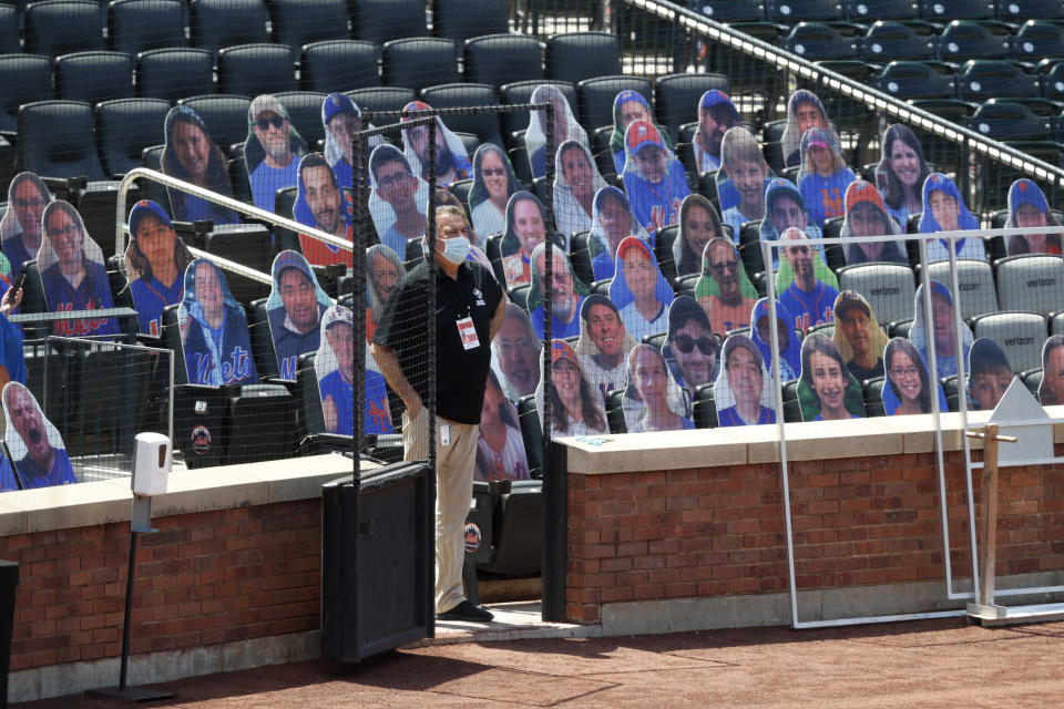 A New York Mets employee stands beside cardboard cutouts of people to simulate of fans in the stands during baseball practice at Citi Field, Thursday, July 16, 2020, in New York. (AP Photo/Kathy Willens)
