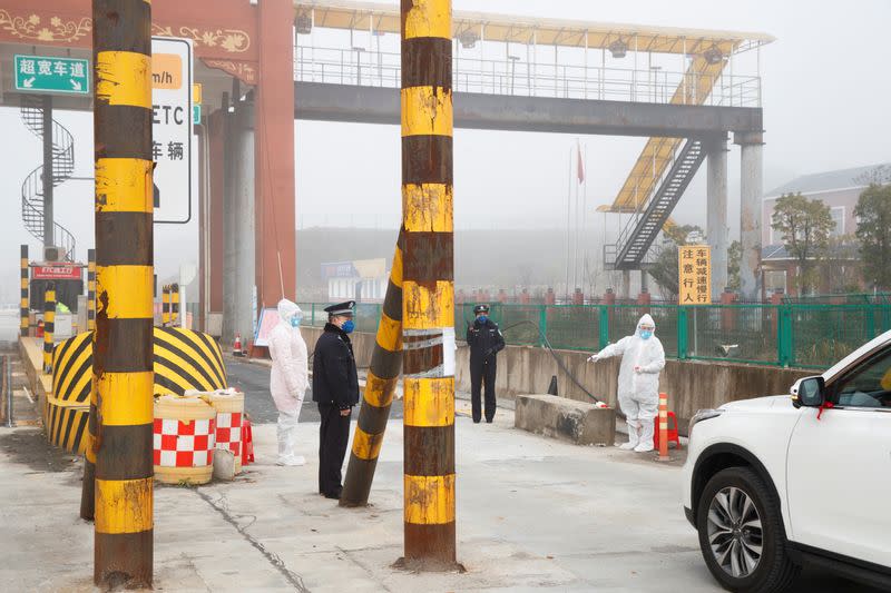 A medical workers in protective suits and police wait for drivers at a checkpoint outside the city of Yueyang