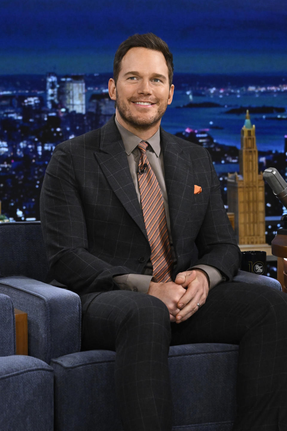 Chris Pratt smiles while sitting on a talk show set