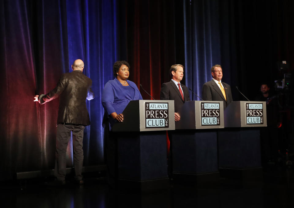 Gubernatorial candidates for Georgia, from left, Democrat Stacey Abrams, Republican Secretary of State Brian Kemp, and Libertarian Ted Metz, right, wait as a stage crew member looks for the source of a fire alarm that sounded during a debate Tuesday, Oct. 23, 2018, in Atlanta. (AP Photo/John Bazemore, Pool)
