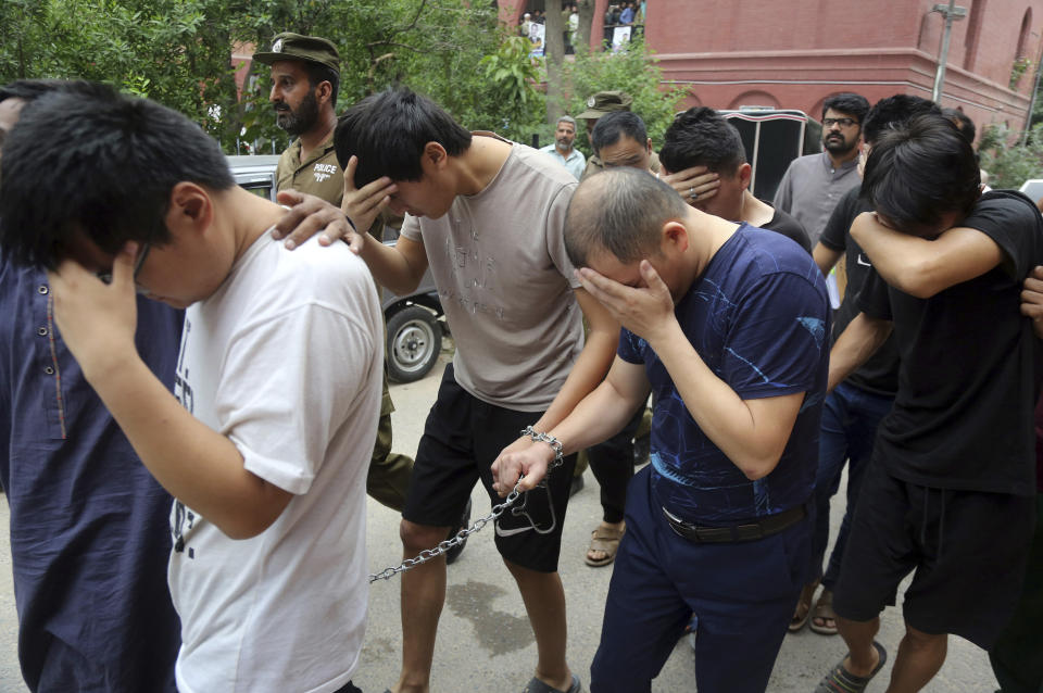 Varios chinos tratan de ocultar sus rostros al llegar a un tribunal de Lahore, Pakistán, donde son juzgados por tráfico de personas. Foto del 11 de mayo del 2019. (AP Photo/K.M. Chaudary, File)