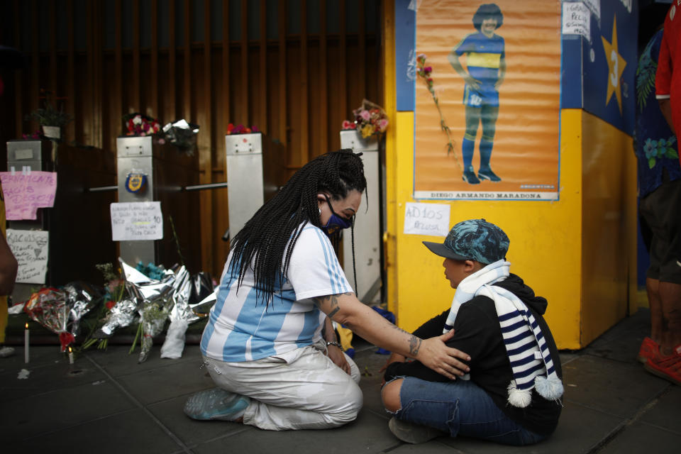 Fans mourn under a poster of Diego Maradona at the entrance of the Boca Juniors stadium, known as La Bombomera, in Buenos Aires, Argentina, Wednesday, Nov. 25, 2020. The Argentine soccer great who was among the best players ever and who led his country to the 1986 World Cup title before later struggling with cocaine use and obesity, died from a heart attack on Wednesday at his home in Buenos Aires. He was 60. (AP Photo/Natacha Pisarenko)