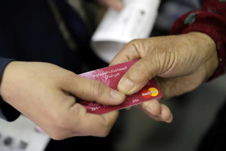 A Syrian refugee presents a World Food Programme debit card to a cashier in a Beirut shop on June 14, 2017