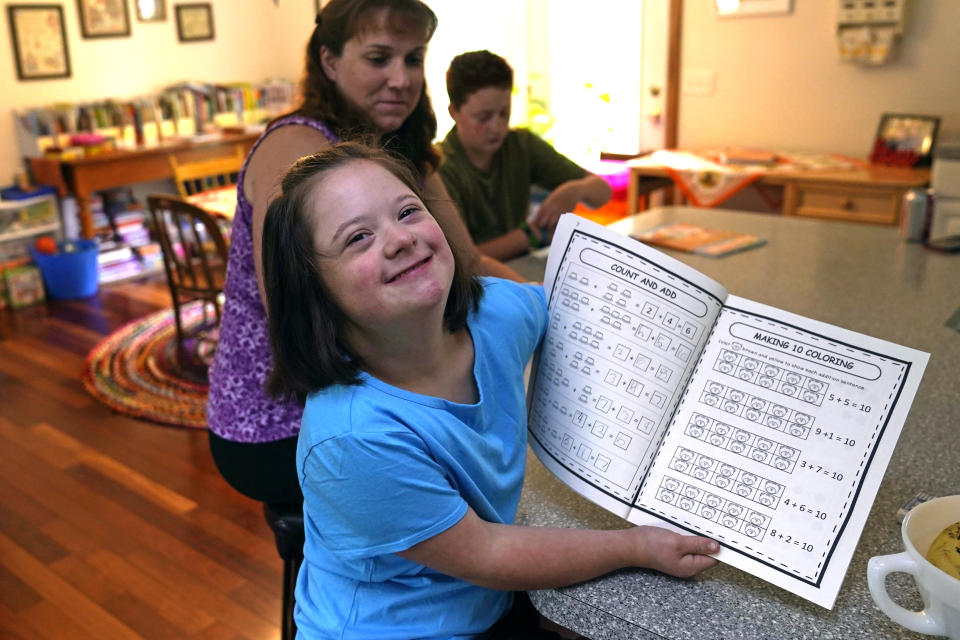 Lily Osgood, 7, who has Down syndrome, shows off her completed work with her mother, Jennifer, and brother, Noah, 12, at their home, Tuesday, July 20, 2021, in Fairfax, Vt. For some families, the switch to homeschooling was influenced by their children’s special needs. Having observed Lily’s progress with reading and arithmetic while at home during the pandemic, Jennifer is convinced homeschooling is the best option for her going forward. (AP Photo/Charles Krupa)