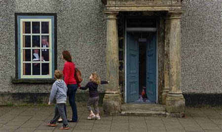 A family walks past an empty building, which has been covered with artwork to make it look more appealing, in the village of Bushmills on the Causeway Coast August 20, 2013. REUTERS/Cathal McNaughton