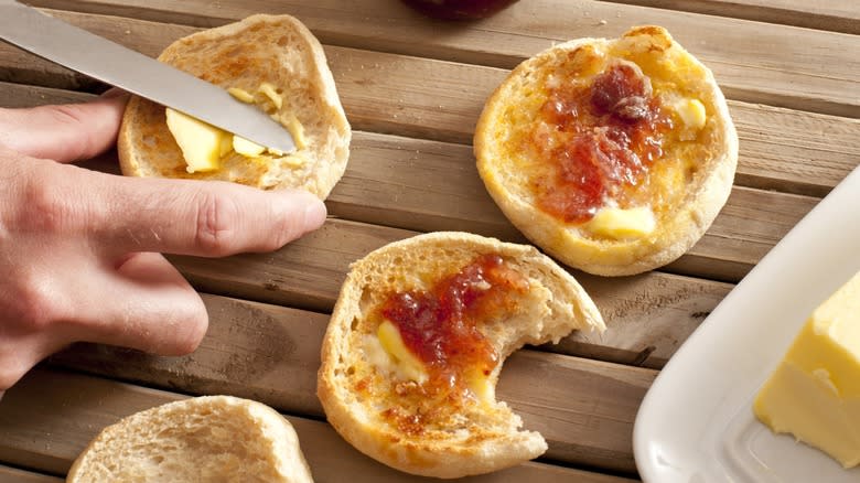 A hand spreading butter and jam on English muffins
