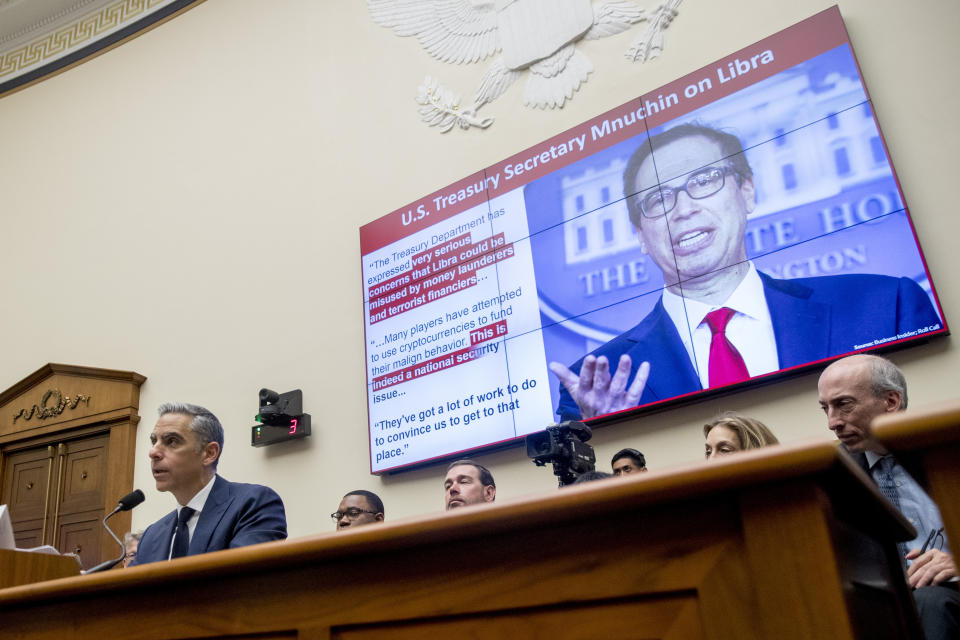 Quotes from Treasury Secretary Steve Mnuchin are displayed on a screen behind David Marcus, CEO of Facebook's Calibra digital wallet service, left, as he speaks during a House Financial Services Committee hearing on Facebook's proposed cryptocurrency on Capitol Hill in Washington, Wednesday, July 17, 2019. (AP Photo/Andrew Harnik)