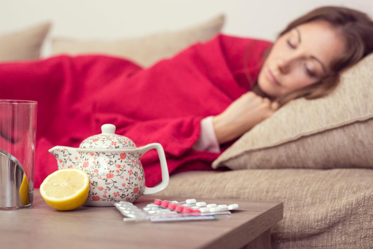 Sick woman sleeping on the couch with medicine and tea on a table