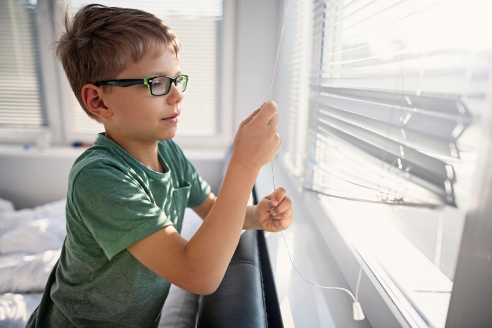 young boy having trouble opening the blinds on a window