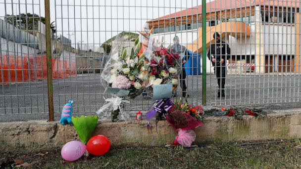 PHOTO: Members of the Guardia di Finanza stand next to floral tributes laid at the fence of PalaMilone sports hall, where victims of a deadly migrant shipwreck are being held, in Crotone, Italy, Feb. 27, 2023. (Remo Casilli/Reuters)