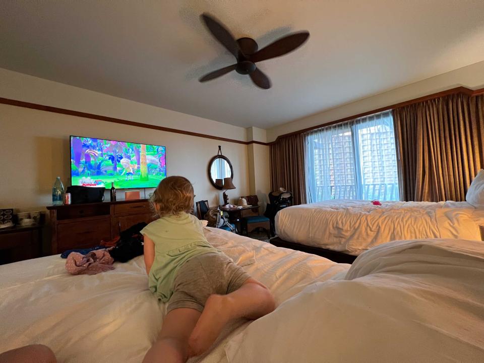 A child laying on a hotel bed watching TV.