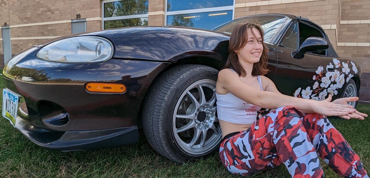 Sam Core, a senior at Liberty High School, relaxes by her Miata convertible during last week’s classic car display she helped organize for her fellow students. She’s geared toward in a career in automotive technologies.