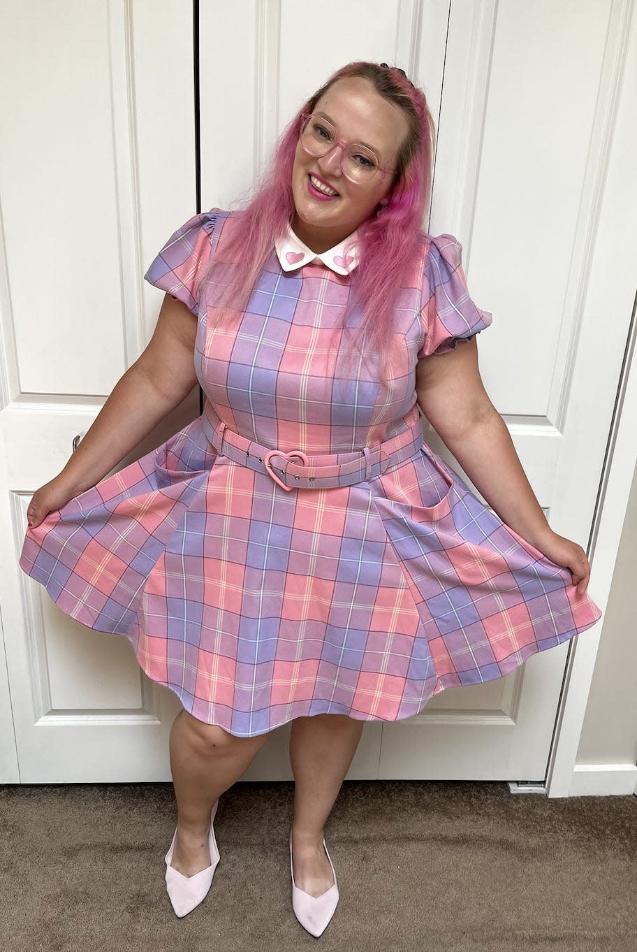 The writer wearing a pink and purple plaid collared dress with pointed light pink shoes