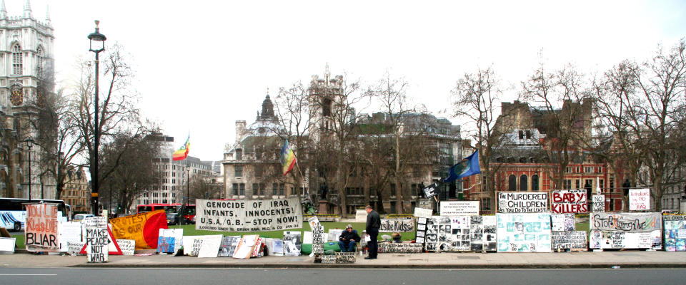 Brian Haw sitting in the centre of a large section of his peace campaign placards, banners and other displays in Parliament Square facing the House of Commons (Richard Keith Wolff/PA)