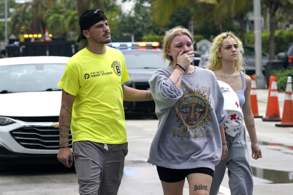 ADDS NAME OF HEVIA'S MOTHER AND THAT SHE DIED IN THE COLLAPSE - Ariana Hevia, of New Orleans, center, walks with Sean Wilt, left, on Friday, June 25, 2021, near the 12-story beachfront condo building that collapsed on Thursday in Surfside, Fla., north of Miami. Hevia's mother, Cassondra Billedeau-Stratton, lived in the building and is listed among those who died in the collapse. (AP Photo/Lynne Sladky)