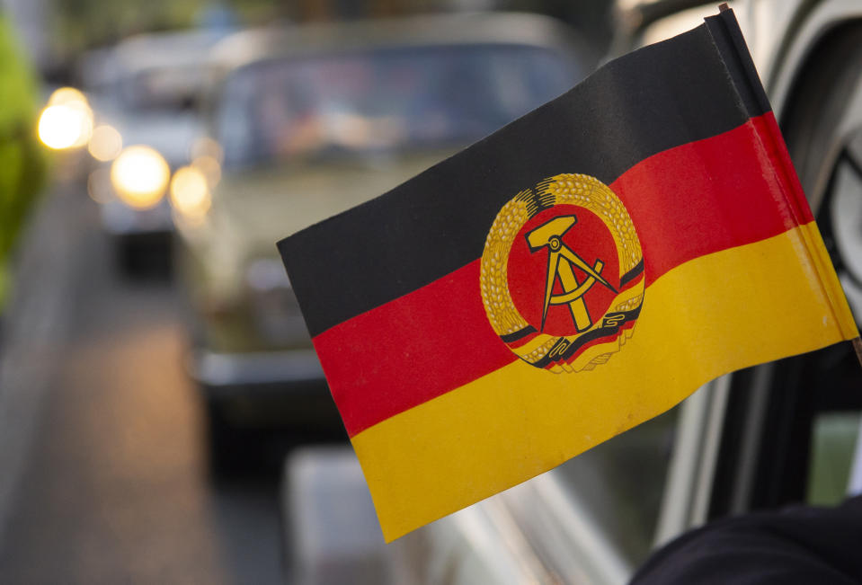 The flag of the former GDR hangs outside of a legendary GDR Trabant (Trabi) cars during a symbolic wall opening, celebrating the 30th anniversary of the falling wall in the outdoor area of the German-German museum in Moedlareuth, Germany, Saturday, Nov. 9, 2019. Moedlareuth, named 'Little Berlin', was the symbol of a divided village along the borderline between East and West Germany. The border ran straight through the little village. (AP Photo/Jens Meyer)