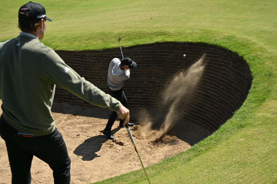 Rasmus Hojgaard (L) watches Denmark's Thorbjorn Olesen play out of a bunker by the 17th green