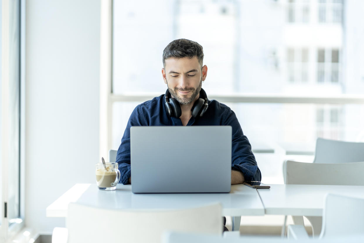 A smiling and confident young man types on his laptop while taking a break.