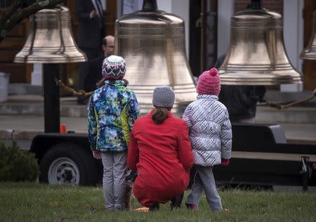 A woman kneels with her children in front of bells which were being rung outside of St. Rose of Lima Church ahead of Sunday service on the two-year anniversary of the Sandy Hook Elementary School shooting in Newtown, Connecticut December 14, 2014. REUTERS/Adrees Latif