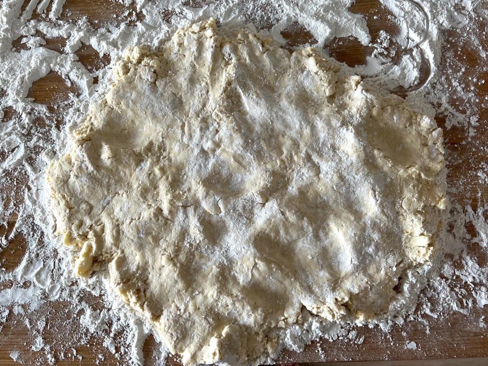 A sheet of dough sits on a wood surface covered in flour.