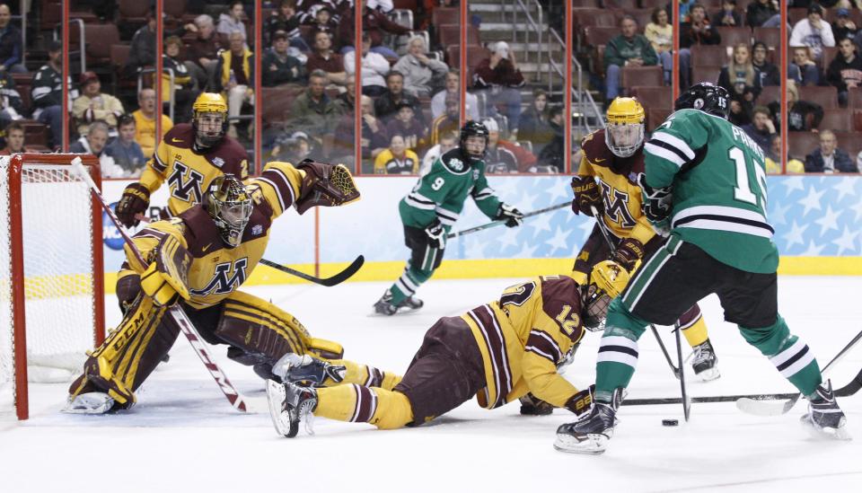Minnesota's Adam Wilcox, left, readies himself as North Dakota's Michael Parks, right, looks to shoot the puck with Minnesota's Justin Holl in front of him during the first period of an NCAA men's college hockey Frozen Four tournament game on Thursday, April 10, 2014, in Philadelphia. (AP Photo/Chris Szagola)