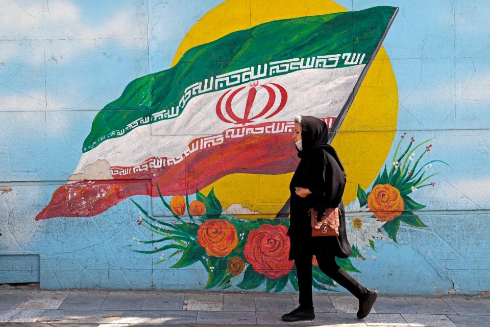 Une femme voilée passe devant un drapeau iranien dans une rue de Téhéran, en Iran, le 11 octobre 2022 - Atta KENARE / AFP